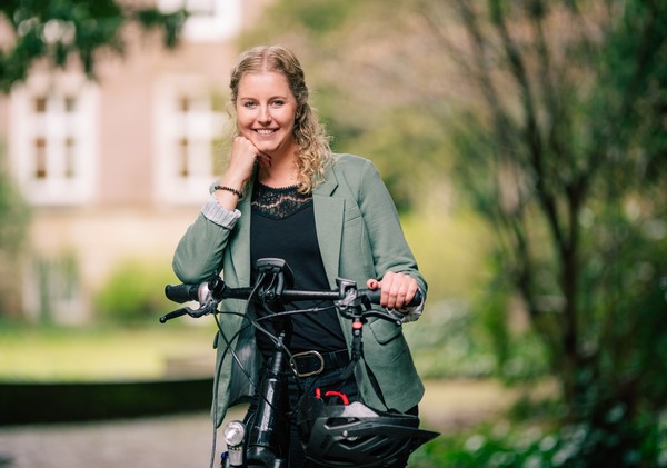 Janine Lammers steht neben ihrem Fahrrad und hat eine Hand auf dem Lenker abgestützt, mit der anderen stützt sie ihr Kinn.
