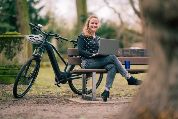 Janina Enning sitzt seitlich auf einer Bank, hinter ihr steht ihr Fahrrad, neben ihr liegt ihr Laptop.