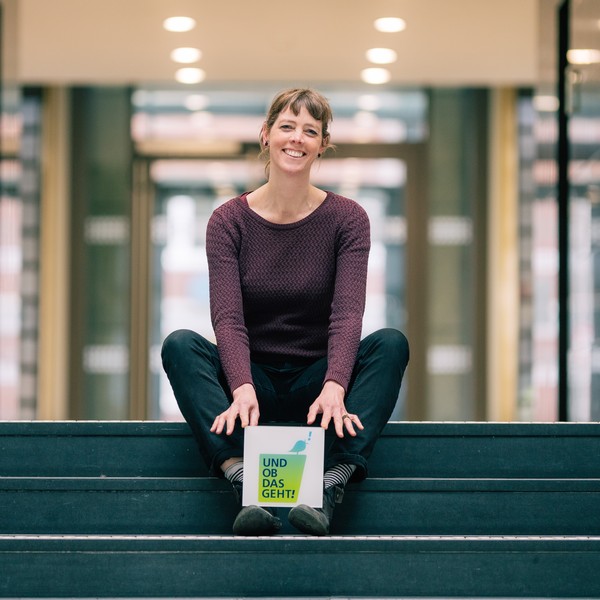Jana Seeg sitzt auf einer Treppe. Die Wort-Bildmarke "Und ob das geht!" steht auf ihren Füßen.