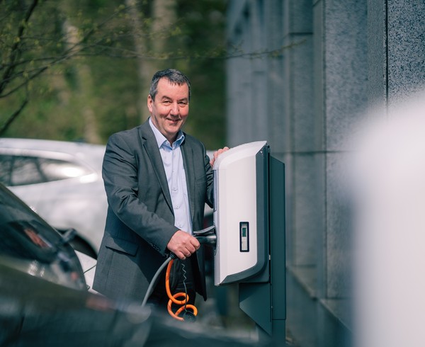 Matthias Gundler steht an einer E-Ladesäule gelehnt und hält ein Ladekabel in der Hand.