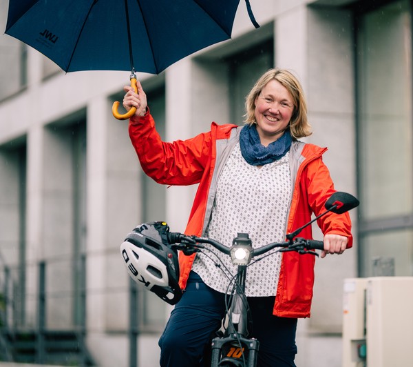 Alexandra Lindstedt sitzt auf ihrem E-Bike und hält freudig einen Schirm in der Hand.